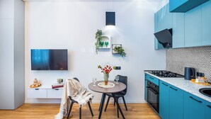 A modern kitchen with teal cabinets, a round dining table, and a flat-screen TV mounted on the wall. - HB apartments Politkovskaia (Tbilisi)