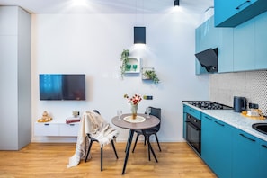 A modern kitchen with teal cabinets, a round dining table, and a flat-screen TV mounted on the wall. - HB apartments Politkovskaia (Tbilisi)