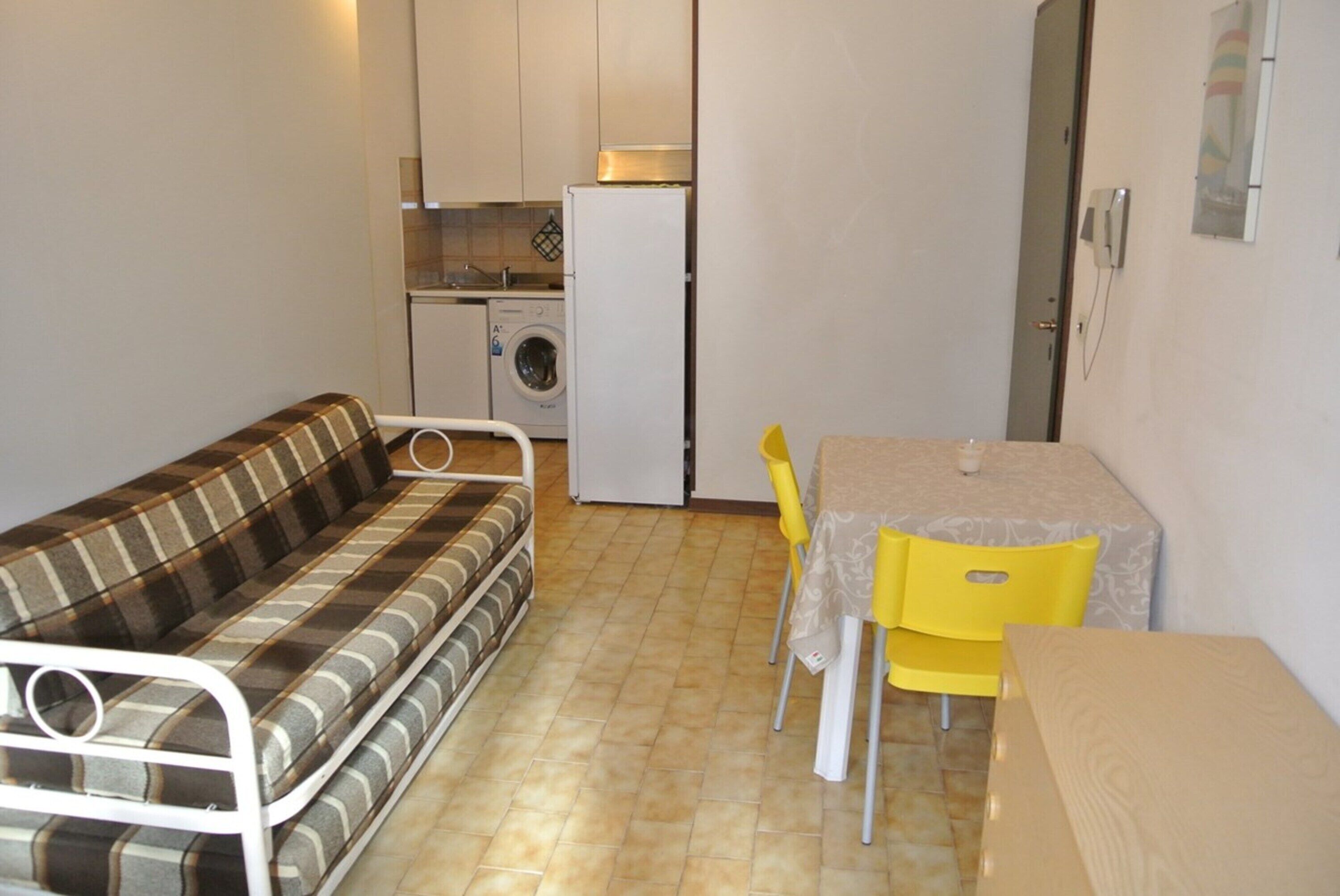 Ett kompakt bostadsutrymme med en soffa, ett litet matbord med stolar, en tvättmaskin och ett kylskåp.