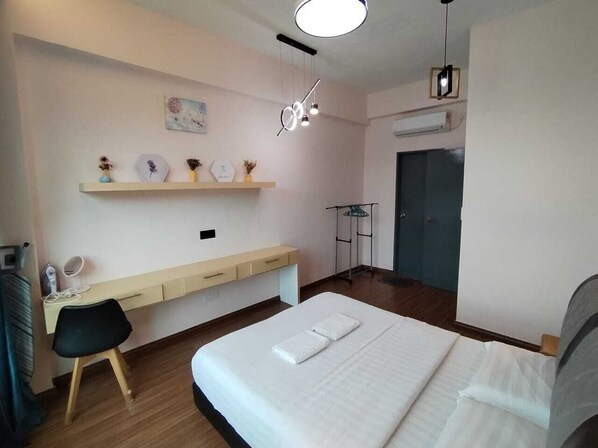 A hotel room with a bed, a desk with a chair, a shelf with decorative items, and a door.