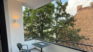 Un balcon avec une table et des chaises, un ordinateur portable et une vue sur les arbres et les bâtiments.