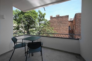 Un balcón con mesa y sillas, vista a árboles y edificios de ladrillo.