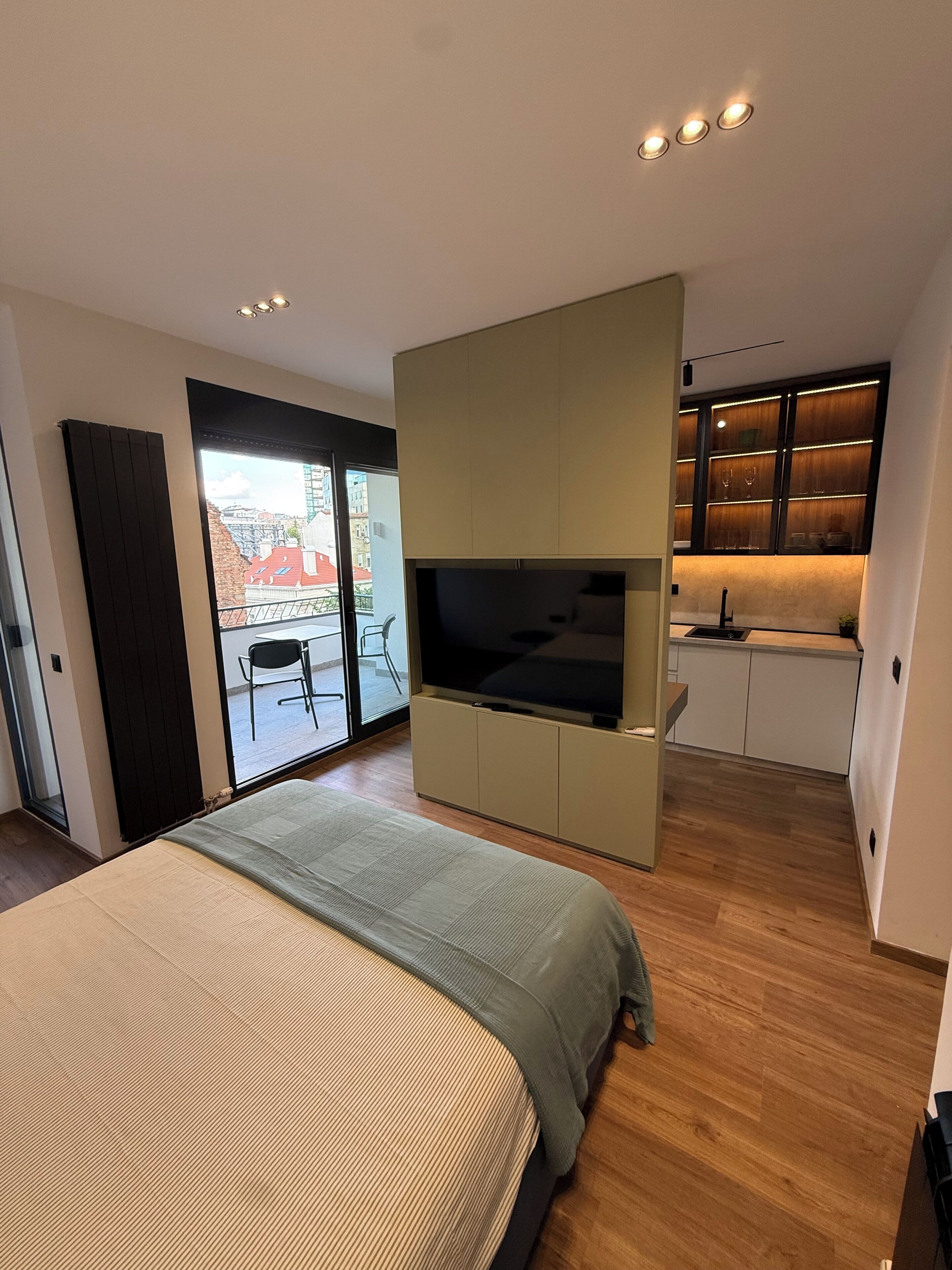 A modern bedroom with a large bed, a TV, and a sliding door leading to a balcony.