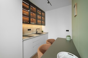 Una cocina moderna con armarios blancos, encimera oscura y estante de madera empotrado con cristalería.