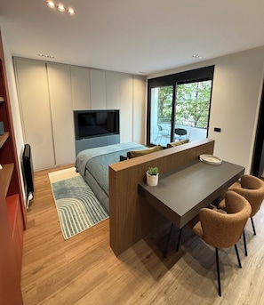A modern bedroom with a bed, a TV, a desk with chairs, and a large window. - Tulum Apart Belgrade 2 (Beograd)