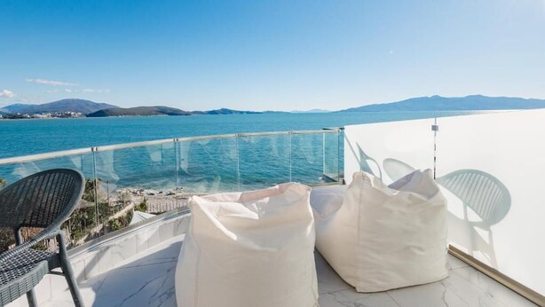 A balcony with a clear view of the sea, a chair, and two white bags. - Hotel Aloha (Sarande)