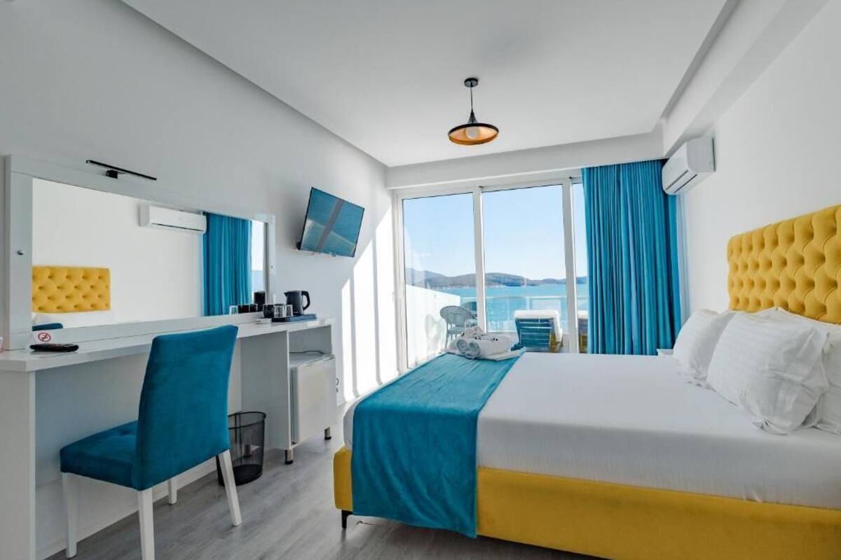 A hotel room with a bed, a desk, a chair, a TV, and a view of the sea.