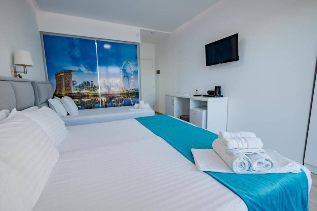 A hotel room with a large bed, a cityscape view, a flat-screen TV, and a desk with a coffee maker.