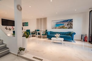 A modern living room with a blue sofa, a white coffee table, and a painting of a coastal landscape.