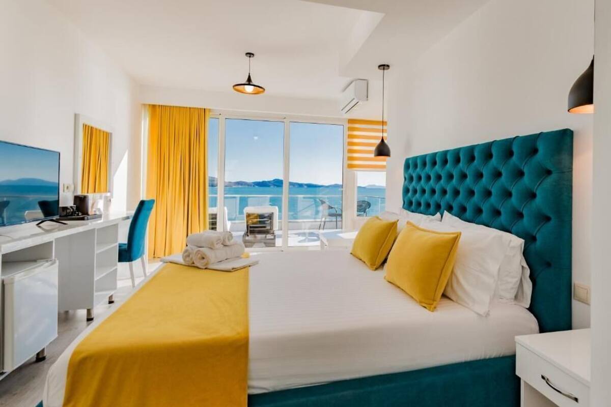A hotel room with a bed, a desk, a chair, a TV, and a balcony with a view.