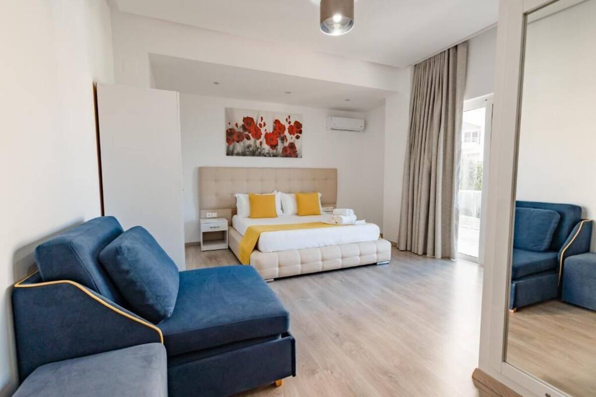 A modern hotel room with a bed, a sofa, a mirror, and a painting on the wall.