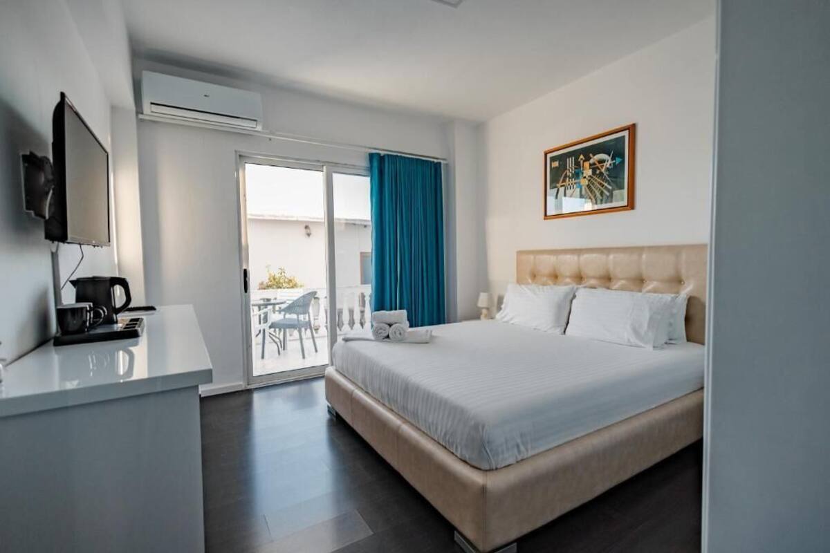A hotel room with a bed, a desk with a coffee maker, a TV, and a sliding glass door to the outside.