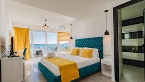 A hotel room with a bed, a desk, a chair, a window with curtains, and a view. - Hotel Aloha (Sarande)