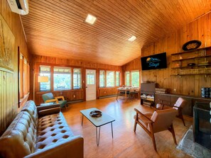 Un interior de madera con sofá, sillones, una mesa, chimenea y televisor.