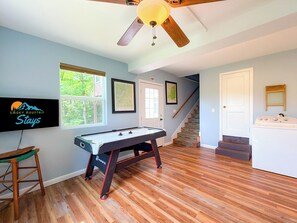 Una habitación con mesa de billar, ventilador de techo, escalera y zona de lavandería.