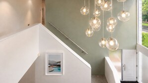 A staircase with a framed picture of a pool, a light green wall, and hanging spherical light fixtures. - Modern coastal retreat – 5 bed home offering space and style for up to 12 guests (Folkestone)
