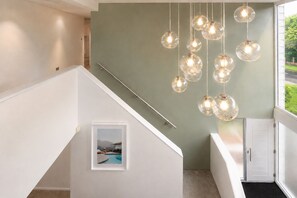 A staircase with a framed picture of a pool, a light green wall, and hanging spherical light fixtures. - Modern coastal retreat – 5 bed home offering space and style for up to 12 guests (Folkestone)