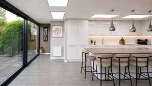 A modern kitchen with a central island, pendant lighting, and a view through large windows. - Modern coastal retreat – 5 bed home offering space and style for up to 12 guests (Folkestone)