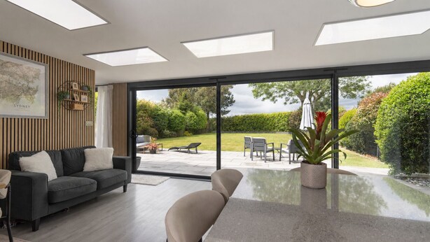 A modern living room with a sofa, chairs, a coffee table, and a large sliding glass door leading to a garden. - Modern coastal retreat – 5 bed home offering space and style for up to 12 guests (Folkestone)