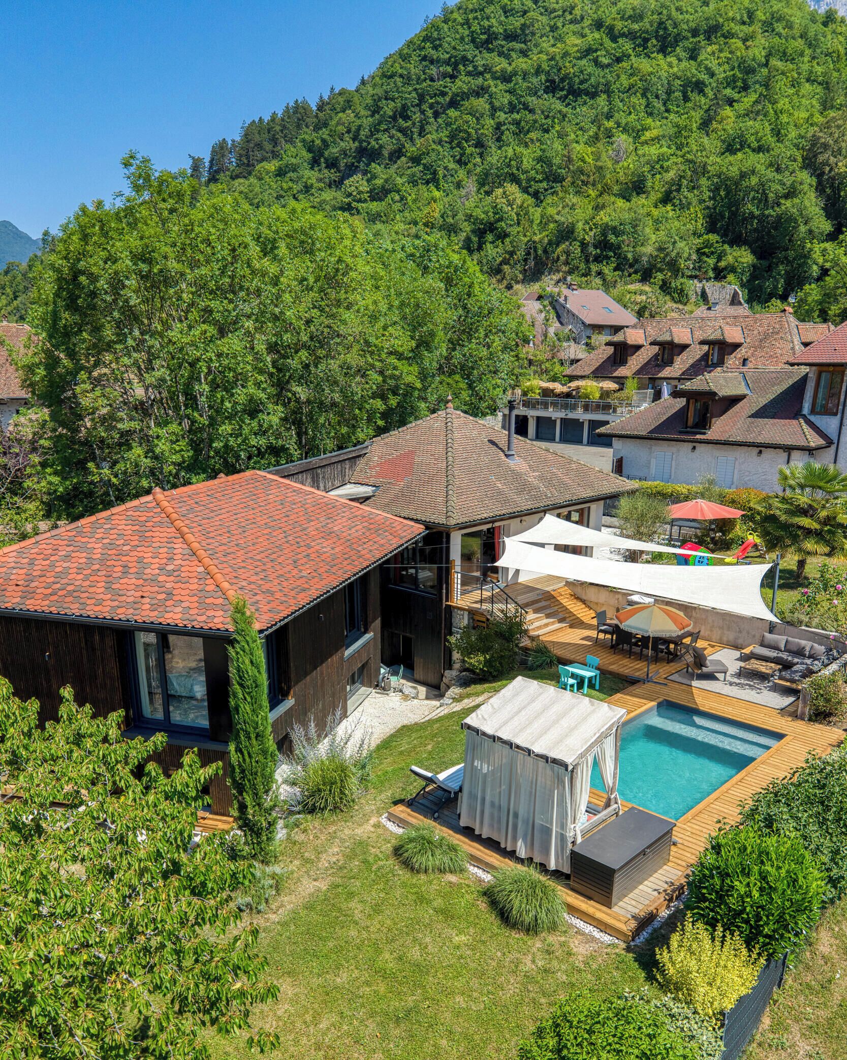 Um imóvel residencial com piscina, área de estar externa e vista para uma colina arborizada.