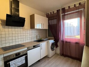 Ett kompakt kök med en inbyggd ugn, en tvättmaskin och ett fönster med gardiner.
