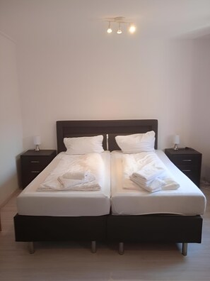 Un lit simple avec une literie blanche, deux tables de chevet et un luminaire au plafond.