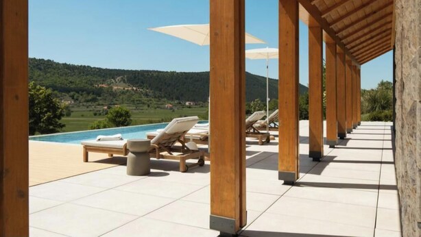 Ein überdachter Außenbereich mit Liegestühlen und Sonnenschirmen mit Blick auf einen Pool und eine hügelige Landschaft.
