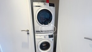 Una lavadora y secadora apiladas en un pasillo, con una puerta a la izquierda.