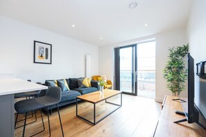 Ein modernes Wohnzimmer mit einer Couch, einem Couchtisch, einem Fernseher und einer Pflanze.