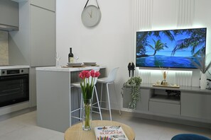 A modern kitchen with a dining area, a clock, a flat-screen TV, and a vase with flowers. - Charming Studio with Stunning Bay Views & Adriatic Soul⁠ (Kriva ulica)
