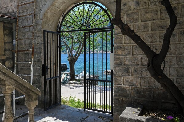 An arched stone doorway with a metal gate, leading to a view of a body of water and a tree. - Charming Studio with Stunning Bay Views & Adriatic Soul⁠ (Kriva ulica)