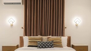 Une chambre à coucher avec un grand lit, deux tables de chevet, un climatiseur fixé au mur et deux appliques murales.