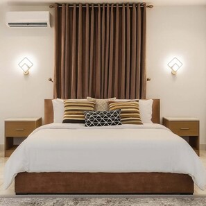 A bedroom with a large bed, two bedside tables, a wall-mounted air conditioner, and two wall sconces. - Nomads Nest Retreat (Abuja)