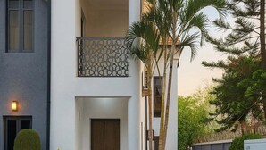 Un bâtiment à deux étages doté d’une porte en bois, d’un balcon orné d’une balustrade à motifs et d’un jardin bien entretenu avec un chemin de pierre.