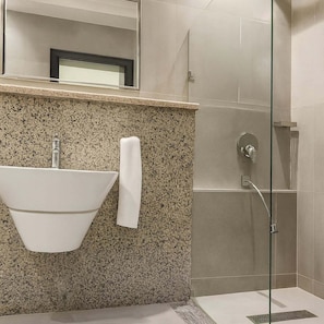 A modern bathroom with a granite countertop, a white sink, a glass shower enclosure, and a mirror above the sink. - Nomads Nest Retreat (Abuja)