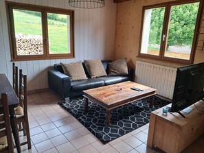Un salon comprenant un canapé, une table basse, un téléviseur et donnant sur l’extérieur.
