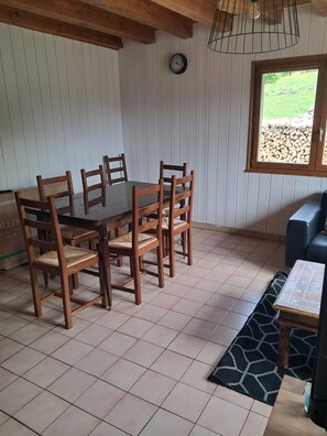Un coin repas avec une table et des chaises en bois, une horloge au mur et une fenêtre donnant sur un jardin.
