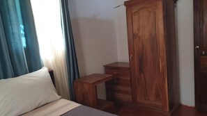 Une chambre à coucher avec un lit, une armoire en bois, une petite table en bois et une fenêtre avec des rideaux.