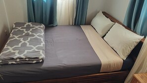 Un lit simple avec un coussin à motifs, une couverture beige et deux oreillers.