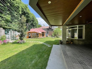 A modern building with a covered patio, a well-maintained lawn, and a brick pathway leading to the entrance. - The Red House (Manali)