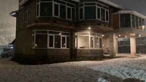 A multi-story house with a snow-covered ground, large windows, and a garage.