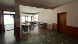 A room with a dining table, chairs, a wooden door, and a view through large windows.