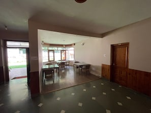 Een kamer met een eettafel, stoelen, een houten deur en uitzicht door grote ramen.