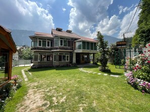 A two-story house with a large front yard, a driveway, and a mountain backdrop. - The Red House (Manali)