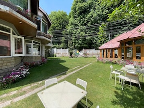 A residential property with a well-maintained lawn, a patio with outdoor furniture, and a stone wall. - The Red House (Manali)