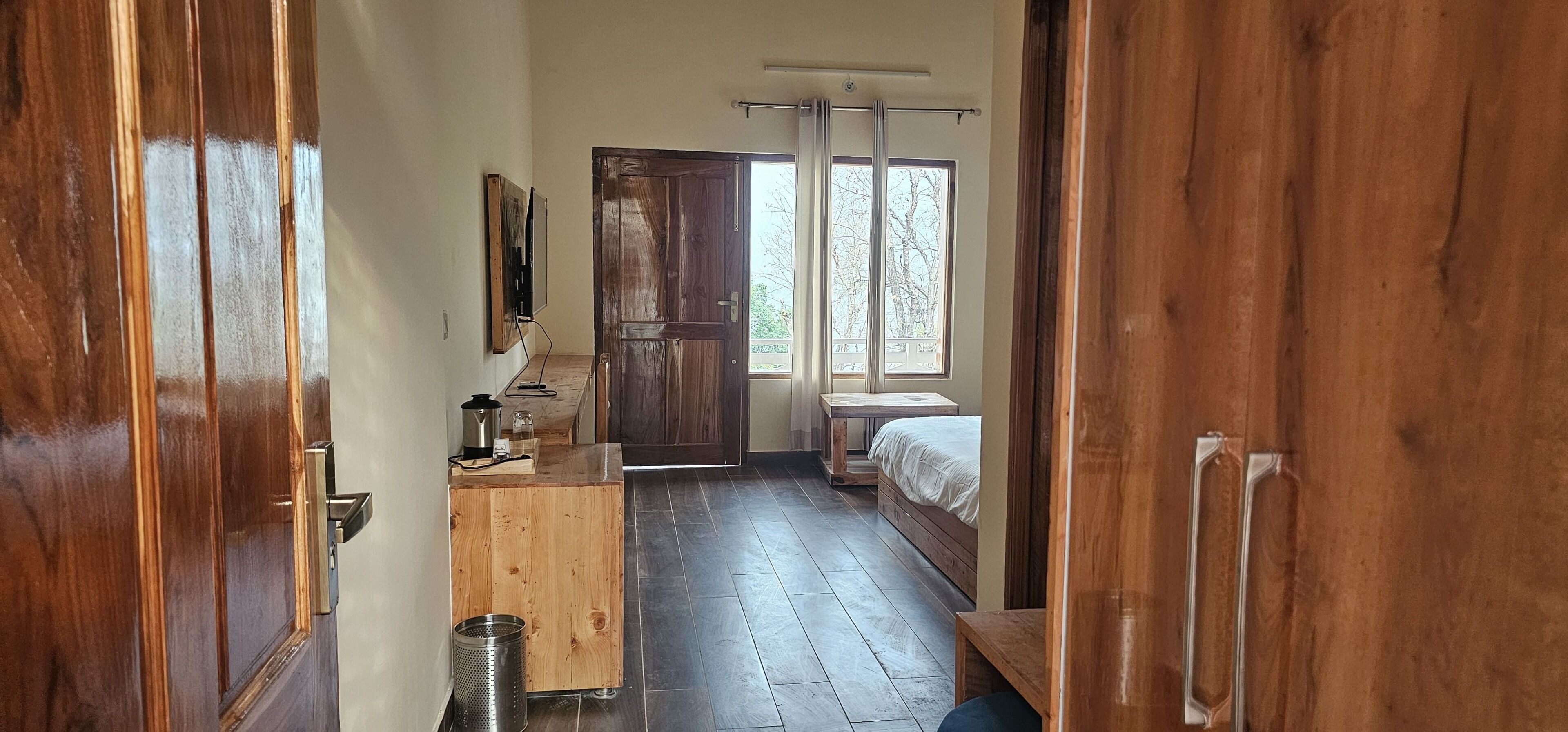 A room with a wooden floor, a bed, a desk with a computer, and a window with curtains.