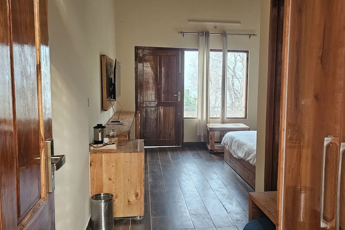 A room with a wooden floor, a bed, a desk with a computer, and a window with curtains.