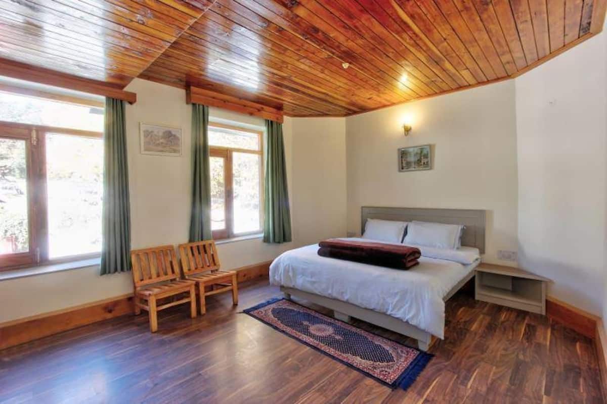 A bedroom with a wooden ceiling, a bed, a nightstand, a chair, and a window with curtains.