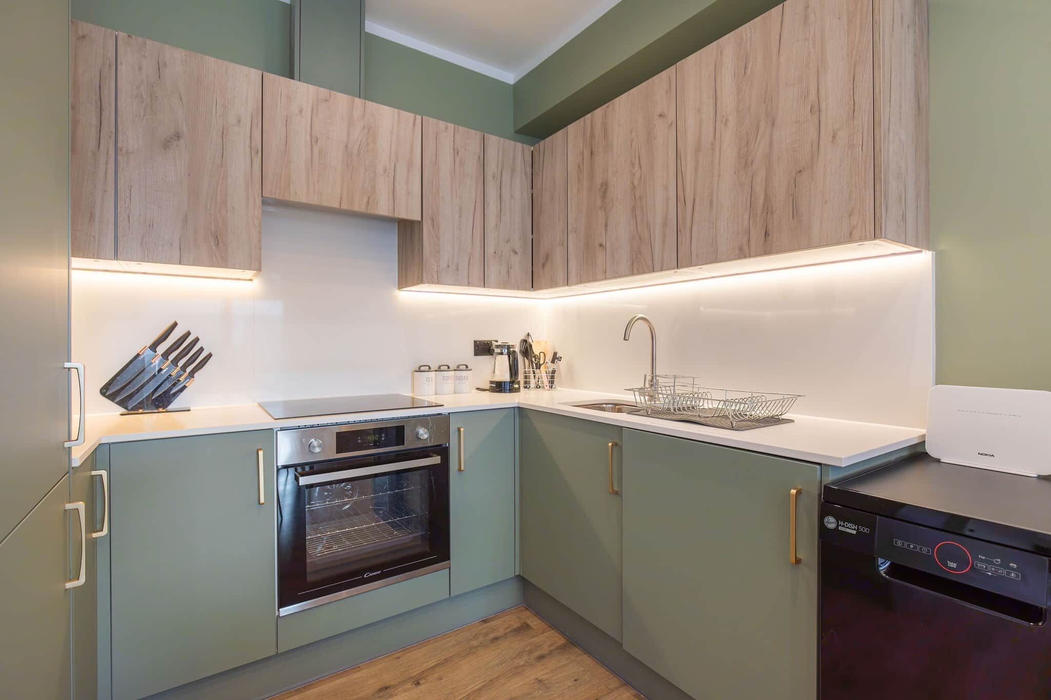 Una cocina moderna con armarios verde claro, horno empotrado, lavavajillas y encimera con un juego de cuchillos y utensilios.