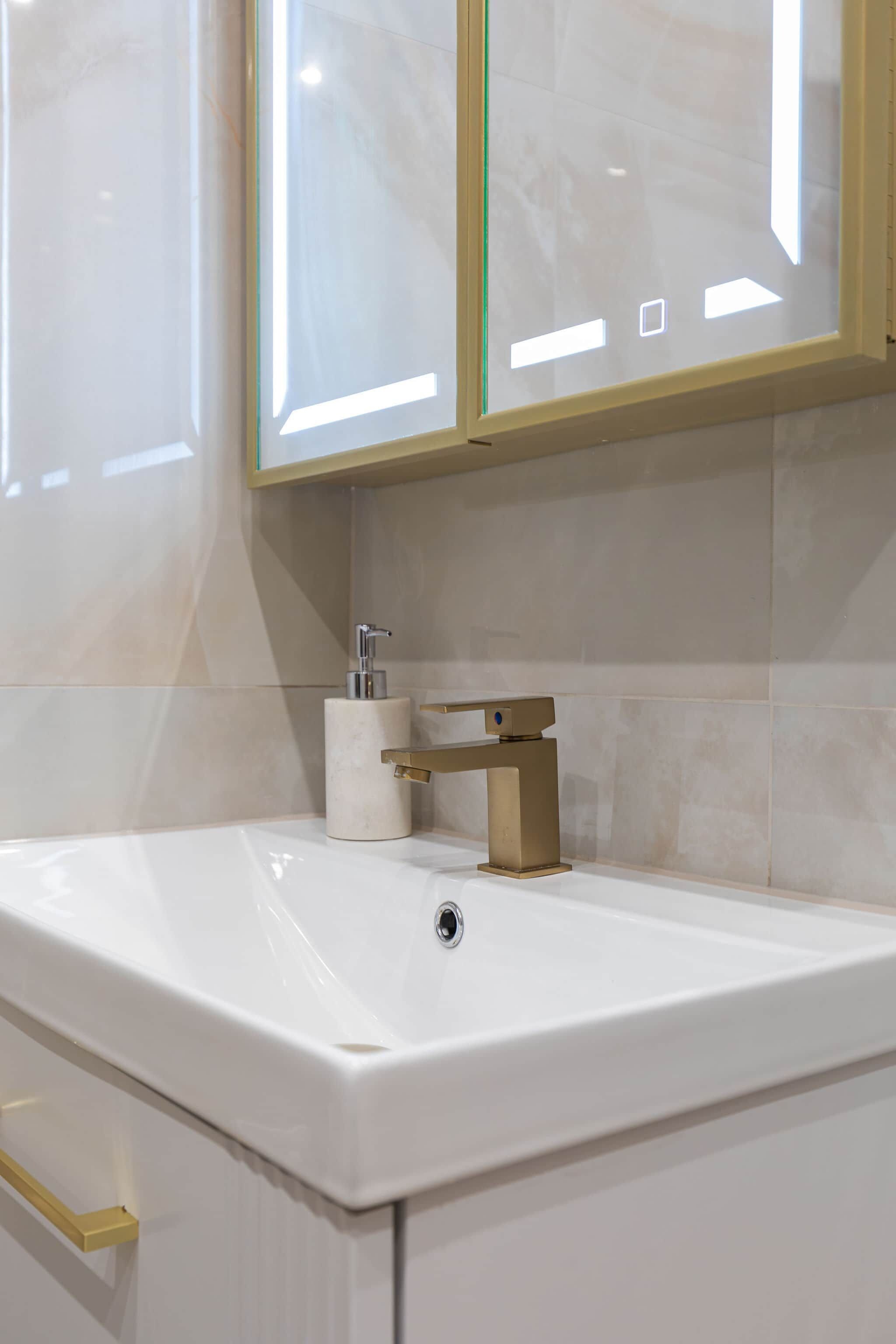 Een badkamer met een witte wastafel, een gouden kraan en marmeren tegels.